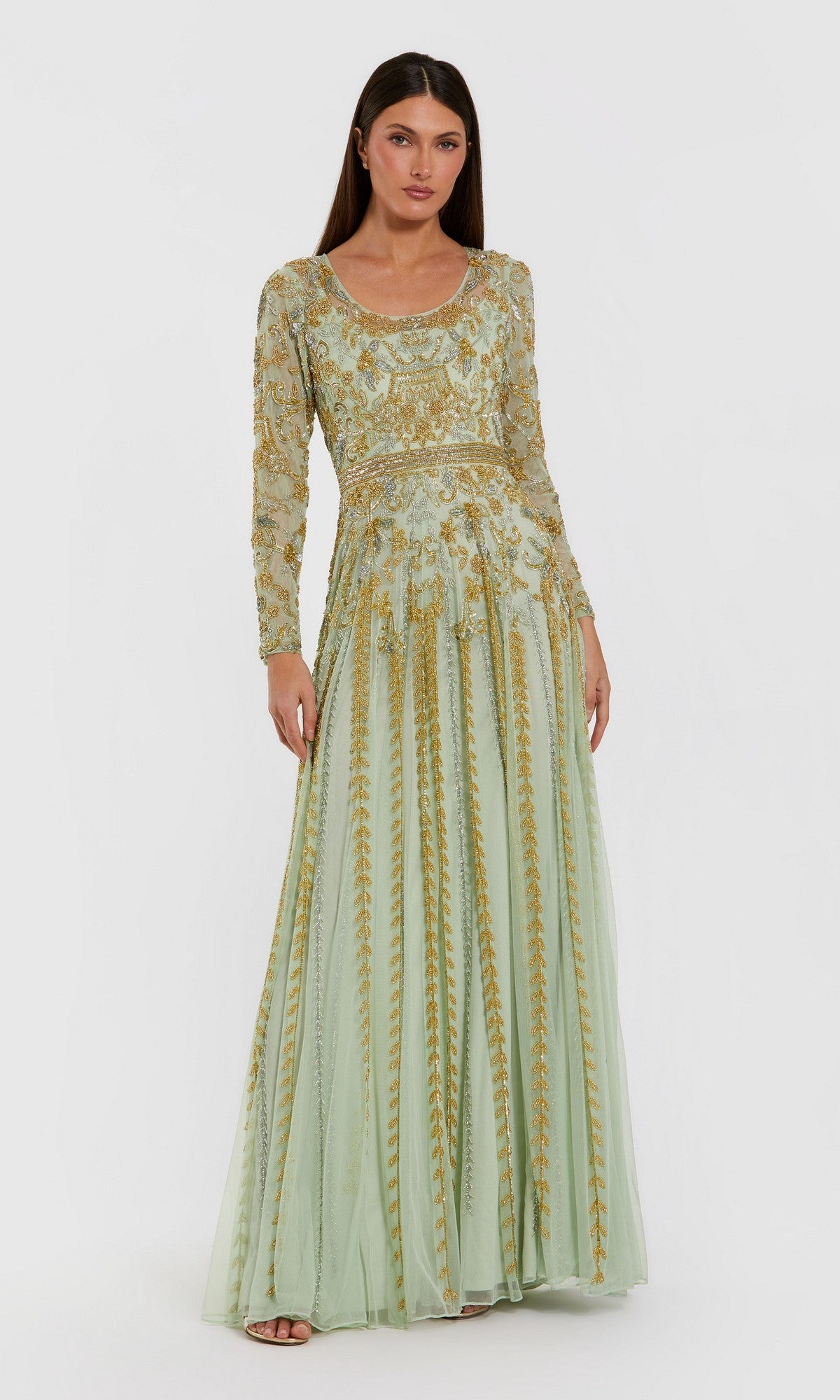 A woman wearing the Mac Duggal 6201 long formal dress in light sage, featuring intricate gold embroidery and delicate gold beaded embellishments, stands against a plain white background.